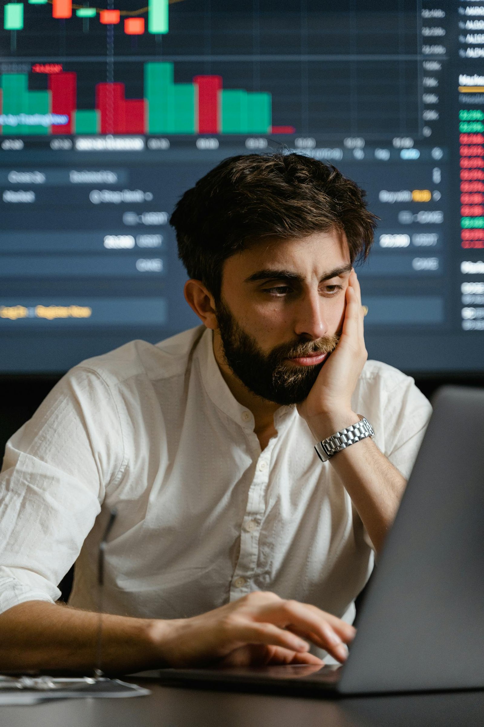 Businessman in office analyzing stock market data on a laptop with a financial chart in the background.